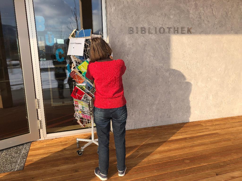 Person von hinten vor einem Drehregal mit Rädern außen vor der Bibliothek